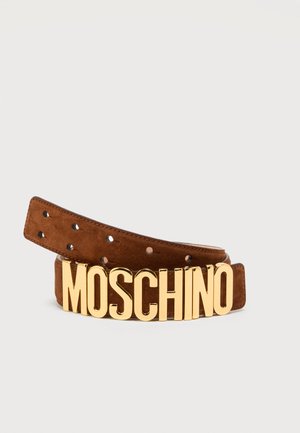 Bruine suède riem met grote gouden letters die "MOSCHINO" spellen als gesp, opgerold tegen een effen lichte achtergrond.