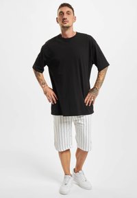 T-shirt en coton noir oversize associé à un short blanc à rayures et des baskets blanches. Manches courtes et coupe décontractée, soulignant le confort.