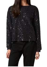 Top de manga larga negro cubierto de lentejuelas negras y plateadas brillantes, con un corte holgado y cuello redondo, combinado con pantalones negros.