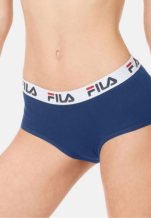 Femme portant des sous-vêtements bleu marine de la marque FILA avec une ceinture élastique blanche, coupés au niveau du ventre et du haut des cuisses.