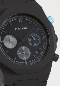Montre analogique noire avec une finition mate, un cadran multifonction, des sous-cadrans gris, des accents turquoise et un boîtier de forme octogonale.