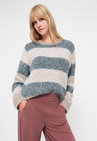 Suéter de malha espesso com largas riscas horizontais em azul e bege, com ombros caídos e um corte descontraído, combinado com calças cor-de-rosa.