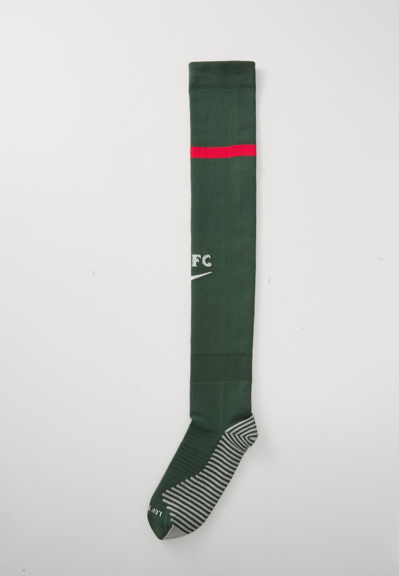 Grüne Fußballsocke mit rotem Streifen, mit dem Nike-Logo und "FC" in Weiß, vor einem schlichten Hintergrund präsentiert. Die Zehenpartie hat ein gestreiftes Design.