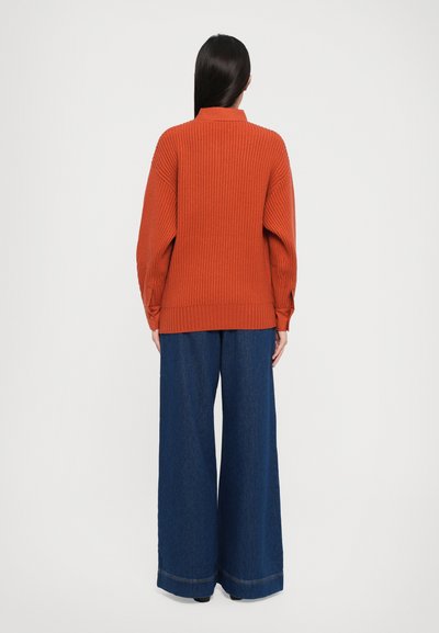 Roestkleurige geribbelde trui met een hoge kraag en verlaagde schouders, gecombineerd met een brede-denim broek in het donker met een omgeslagen zoom.