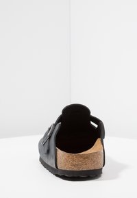 Sandale en cuir noir, design à enfiler, semelle en liège, surface texturée, arrière ouvert et découpes latérales pour la respirabilité.