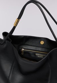 Schwarze Ledertasche mit glatter Textur, ausgestattet mit einem goldfarbenen magnetischen Druckknopfverschluss und einer Innenfach mit Reißverschluss.