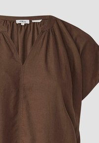 Bruine, lichte top met een V-hals en geplooide details op de schouders. Zachte textuur, korte mouwen en een ontspannen pasvorm.