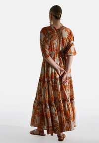 Maxikleid aus leichtem Stoff mit orangen Blumenmuster auf beiger Hintergrund, mit gestuften Design und elastischem Bund. Bindeband im Rücken.