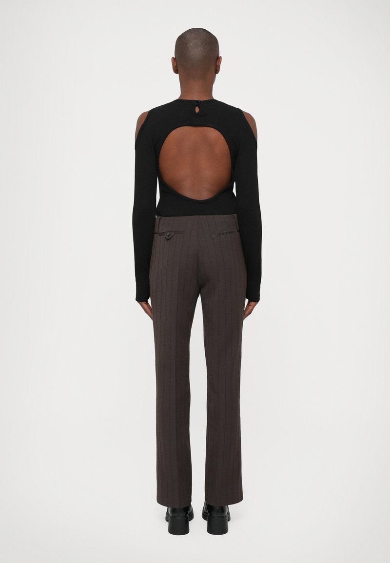 Haut noir à manches longues avec un dos ouvert, associé à un pantalon marron à rayures. Le pantalon présente un détail de bouton à la taille.