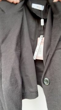 Svart kort blazer i texturerat tyg, med rund knäppning, tagg med varumärkeslogotyp och en enkel kragsdesign.