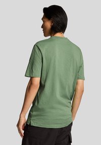 T-shirt a maniche corte con scollo rotondo verde oliva, in tessuto testurizzato con spacchi laterali per facilitare i movimenti. Nessun motivo o grafica particolare.