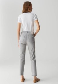 Jeans grigi con vestibilità dritta, caratterizzati da una vita media, tasche posteriori e un'etichetta bianca sulla cintura. Combinati con una t-shirt bianca.