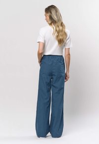 Plave hlače širokih nogavica s elastičnim pojasom, izrađene od laganog materijala. Uparene s bijelom, rebrastom majicom kratkih rukava.