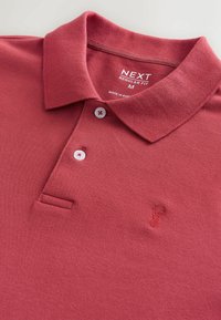 Tricou polo roșu din material texturat. Are guler, trei nasturi și un mic logo brodat pe partea stângă. Croială normală.