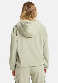 Hellgrüner Fleece-Hoodie mit einer geräumigen Kapuze, strukturiertem Stoff und einer lockeren Passform. Verfügt über abfallende Schultern und gerippte Bündchen.