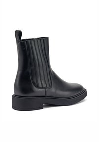 Stivale alla caviglia in pelle nera con pannelli laterali elasticizzati a costine, punta arrotondata e suola piatta. Caratterizzato da un pratico tassello sul retro per facilitare l'indossamento.