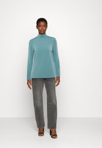 Camisola de gola alta em azul claro com mangas compridas, combinada com jeans cinzentos de perna reta de cintura alta e sapatos de salto abertos pretos. Design simples.