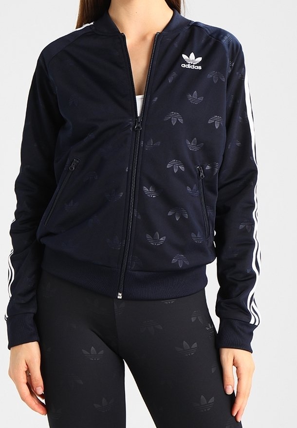 Marinblå bomberjacka med dragkedja och tonade Adidas-logotyper, vita ränder längs ärmarna, ribbade ärmslut och en slät syntetisk textur.