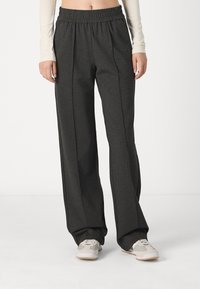 Pantalones de pierna ancha de color gris carbón con una cinturilla elástica, que cuentan con costuras laterales y un tejido suave y texturizado. Combinados con zapatillas de color claro.