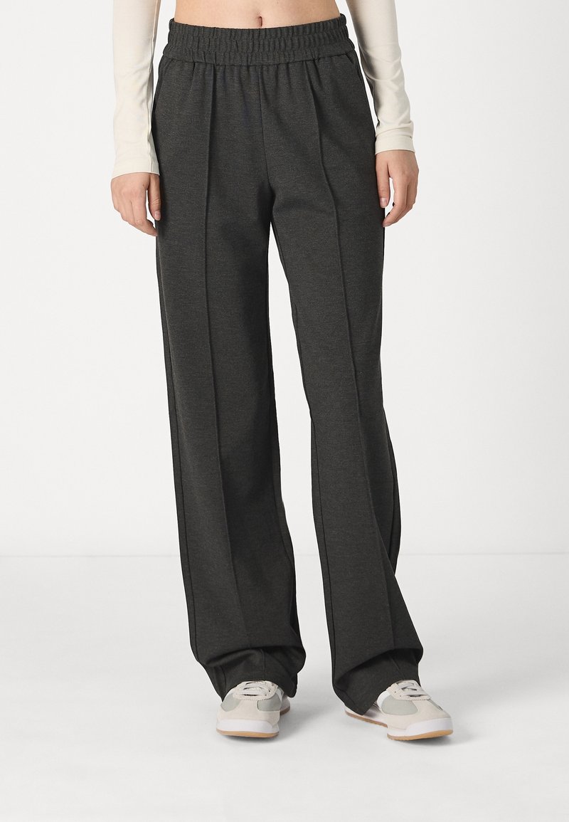 Pantalones de pierna ancha de color gris carbón con una cinturilla elástica, que cuentan con costuras laterales y un tejido suave y texturizado. Combinados con zapatillas de color claro.