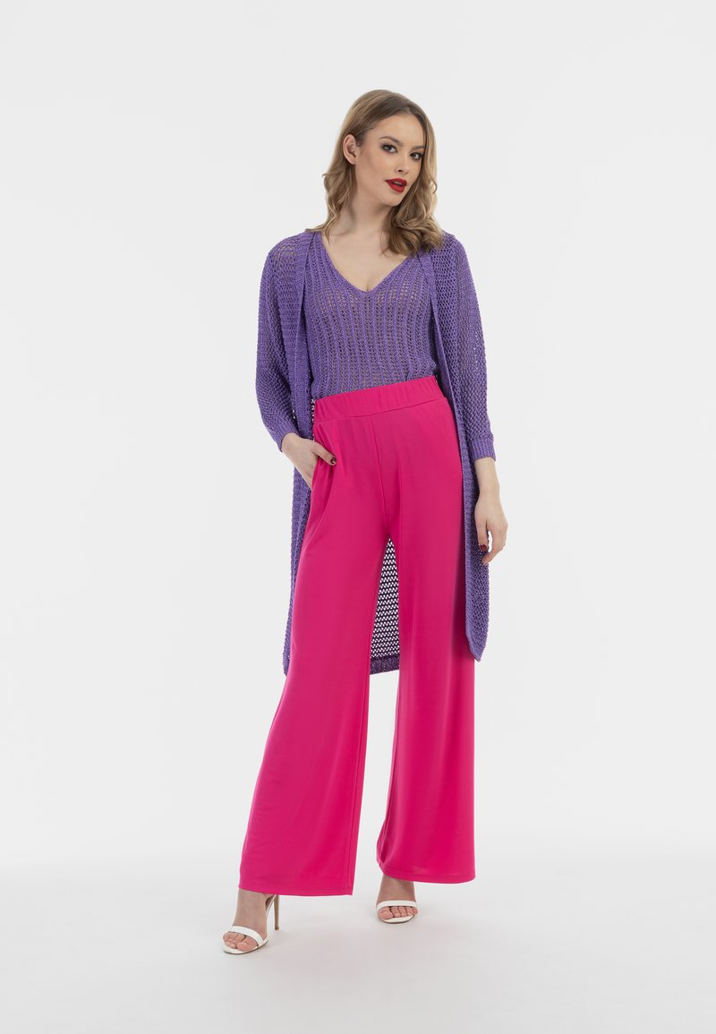 Un cardigan tricotat violet peste un top violet ajustat și pantaloni largi roz. Ținuta are un model texturat și un design fluid.