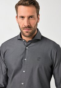 Camicia grigia con bottoni, caratterizzata da un motivo testurizzato, con colletto, sei bottoni e un piccolo logo ricamato sul lato sinistro.