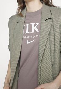 Blazer grigio a scacchi sopra una maglietta Nike color malva con logo bianco. Il blazer presenta rever strutturati e apertura frontale. Tessuto a trama liscia.