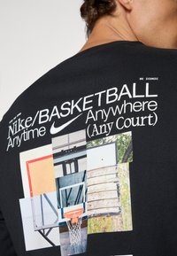 Sort sweatshirt med grafiske tryk af basketballkurve og baner, med tekst der læser "Nike/BASKETBALL Anytime Anywhere (Any Court)."