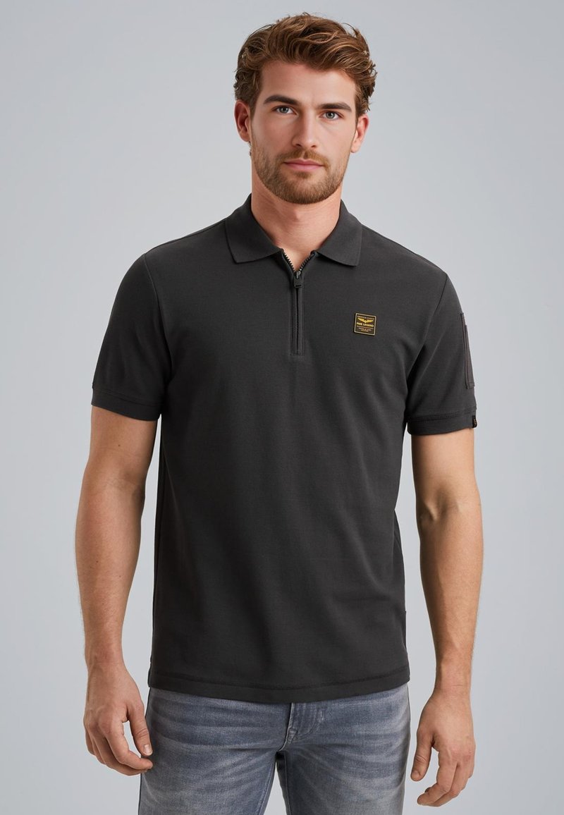 Zwart polo shirt met korte mouwen, ritskraag en een klein geel logo-opdruk op de borst. Draag het met lichtblauwe denim jeans.