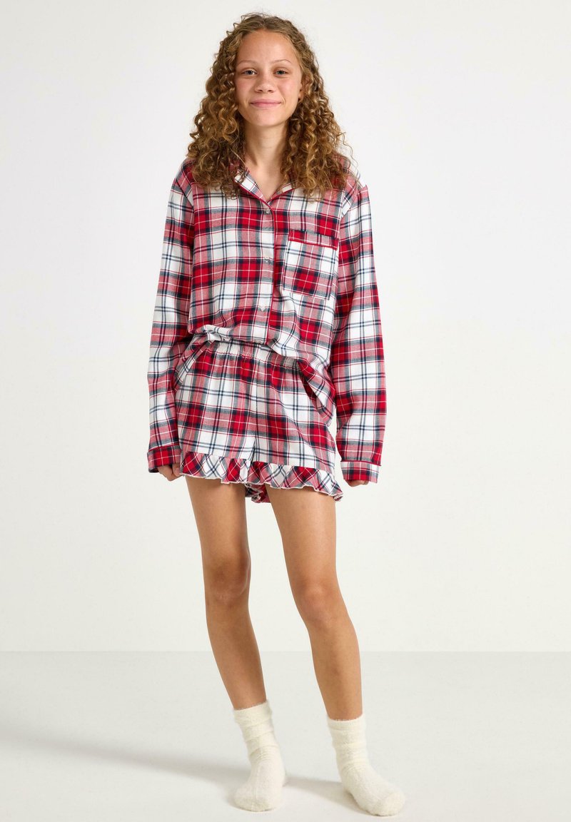 Ensemble de pyjama à carreaux rouges et blancs en tissu doux ; comprend une chemise à manches longues avec boutons et un short à volants. Chaussettes blanches douces.
