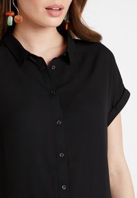 Black short-sleeve shirt made of smooth fabric, featuring a pointed collar and front button closure. Subtle sheen and no prominent patterns.