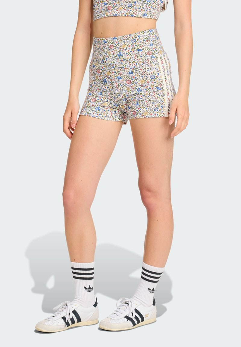 Květinový crop top a šortky s vysokým pasem z měkké látky. Obsahuje barevné květinové vzory, kontrastní boční pruhy a sportovní obuv.