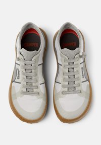 Baskets de sport blanches et grises avec une tige en maille texturée, des lacets gris et une semelle en caoutchouc marron. "CAMPER" imprimé sur la semelle intérieure et sur le côté.