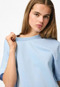 Gaiši zils īsās piedurknes T-krekls, izgatavots no mīkstas auduma. Piedāvā brīvu piegriezumu ar apaļu kakla izgriezumu un nedaudz nolaižamajām plecu šuvēm.