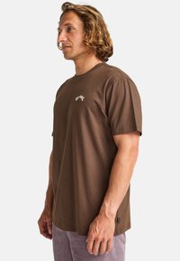 Brun bomulds T-shirt med rund hals og korte ærmer. Har et lille broderet logo på brystet og en lige kant.