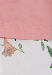 Roze katoenen top met een ronde halslijn, gecombineerd met witte stof met bloemenpatronen in groen en roze. Stiksels zijn zichtbaar.