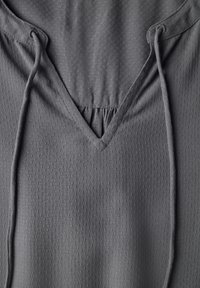 Suéter gris con escote en V y cordones ajustables. Fabricado con un material texturizado que presenta pequeños puntos. Tela suave y transpirable.
