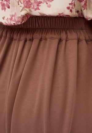 Elastische tailleband van een bruine rok gecombineerd met een roze bloemenblouse, waarbij de textuur van de stof en de plooien van het kledingstuk zichtbaar zijn.