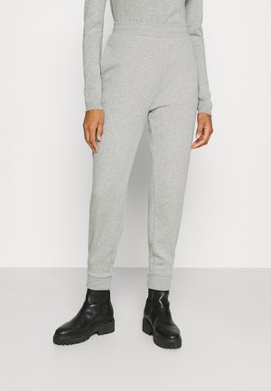 Person trägt hellgraue Jogginghose und schwarze klobige Stiefeletten, steht vor einem schlichten hellen Hintergrund.