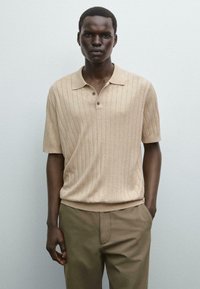 Beige ribbet polo skjorte med krave og tre knapper, parret med olivengrønne bukser. Glat tekstur og afslappet pasform.
