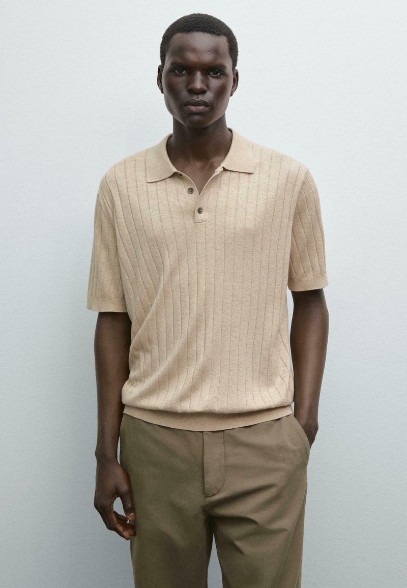 Beige ribbet polo skjorte med krave og tre knapper, parret med olivengrønne bukser. Glat tekstur og afslappet pasform.