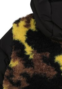 Giacca puffer con esterno in nylon nero e una parte frontale morbida e decorata in tonalità di giallo, marrone e nero con una finitura testurizzata.