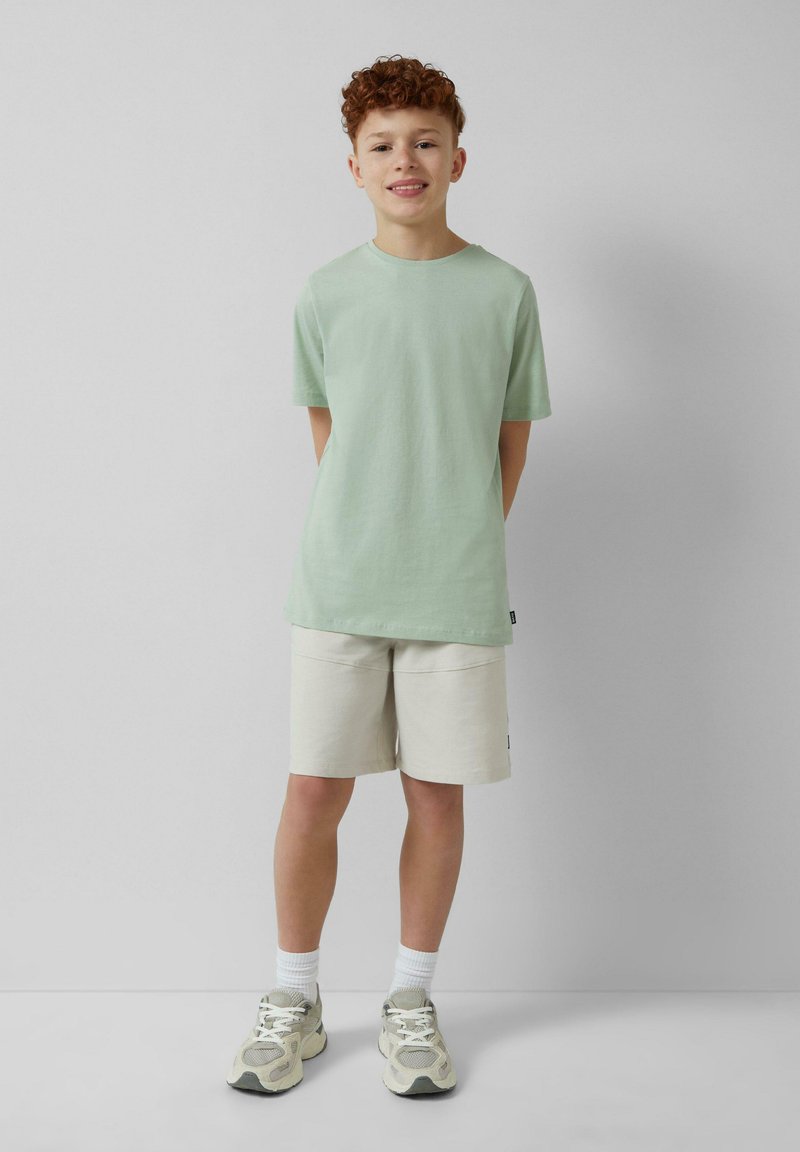 Mintgroene T-shirt met korte mouwen, gecombineerd met witte shorts, met een relaxte pasvorm. Gestyled met lichtgrijze sneakers en witte crew-sokken.