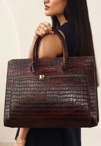 Brown croc-embossed leather tote bag with double handles, featuring a front pocket and gold-tone hardware accents.