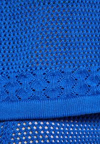 Țesătură tricotată de culoare albastră, având un model de plasă. Designul include o bandă texturată cu o margine ondulată în partea de jos.