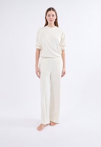 Conjunto de loungewear crema que incluye una camiseta de manga larga de corte relajado y pantalones de pierna ancha, fabricado en un tejido suave y liso con un diseño minimalista.