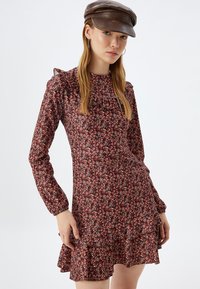 Blumenkleid mit langen Puffärmeln, gerafftem Ausschnitt und gestuftem Rock. Der Stoff hat einen dunklen Hintergrund mit kleinen verstreuten Blumen.