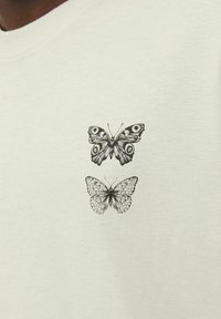 Light gray t-shirt featuring black illustrations of two butterflies, one above the other, on the left chest area. Soft cotton fabric.