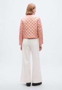 Ροζ μπουφάν bomber με καπιτονέ υφή και γυαλιστερό φινίρισμα, cropped σχεδιασμό, φαρδιά μανίκια και στρογγυλή γιακά, συνδυασμένο με λευκό ψηλόμεσο παντελόνι.