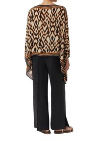 Lekki, wzorzysty poncho w kolorze kremowym z brązowymi i czarnymi geometrycznymi wzorami, o luźnym kroju i asymetrycznym dołem. W połączeniu z czarnymi spodniami.